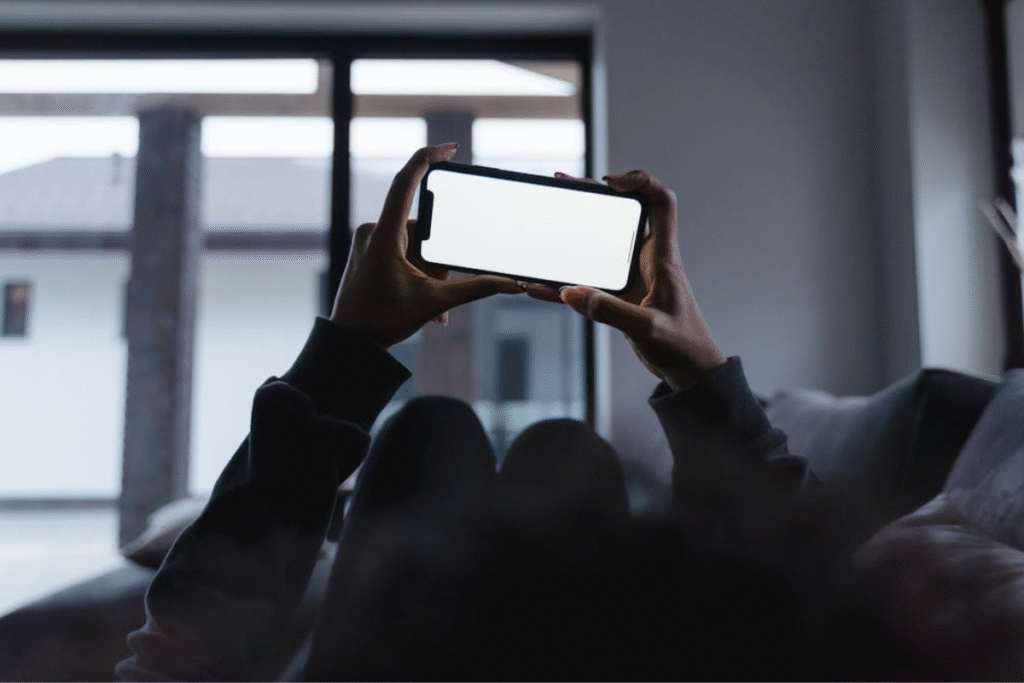 A person relaxing on a couch while holding a smartphone with a blank white screen, ideal for showcasing a mindfulness app interface.