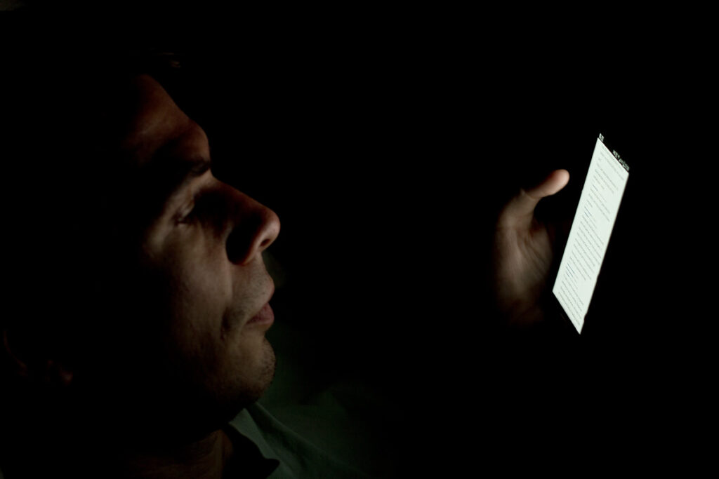 Person using a smartphone in a dark room, illustrating how blue light exposure before bed disrupts sleep quality, increases insomnia, and affects mental wellness